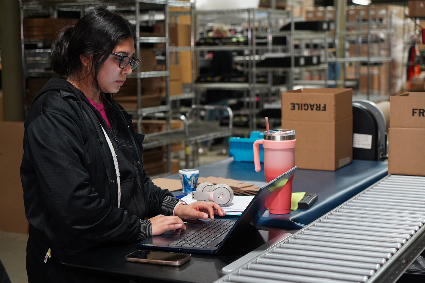 Woman confirming shipping addresses on computer in front of conveyor 